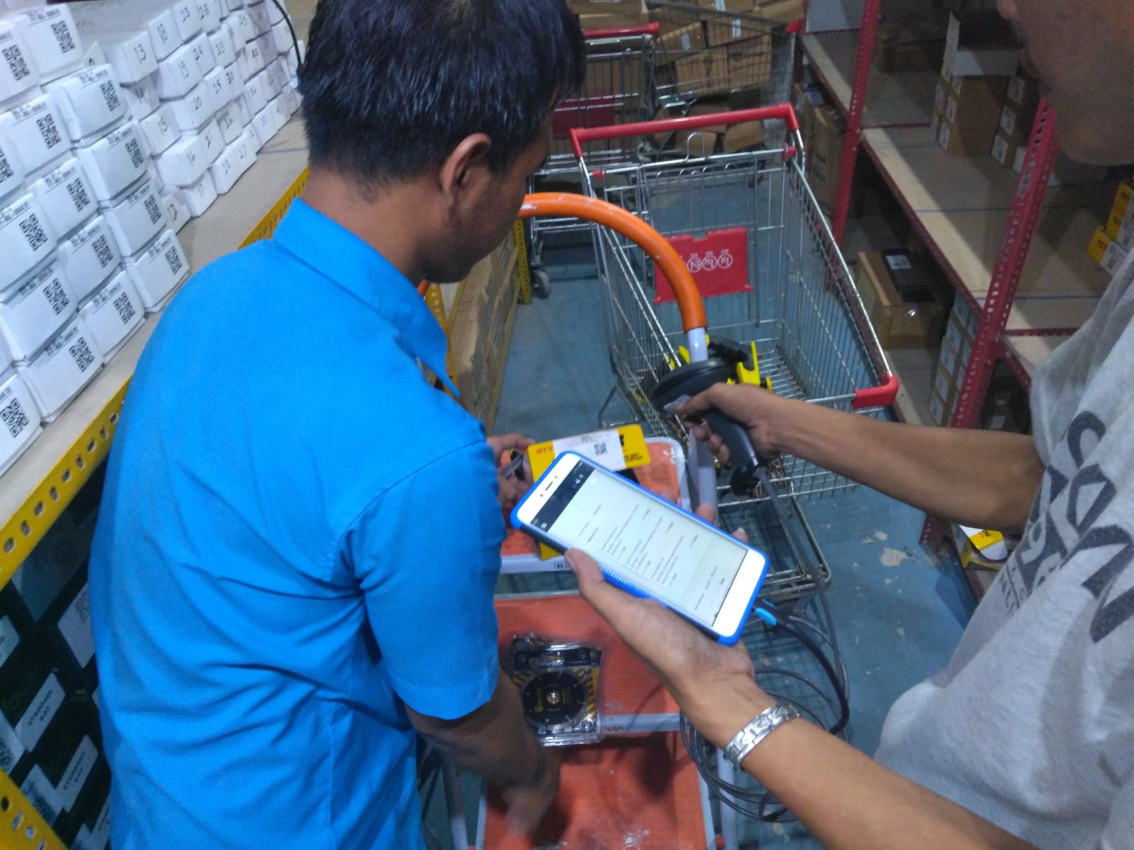 Dua petugas melakukan stock opname di rak gudang dengan scanner dan aplikasi mobile